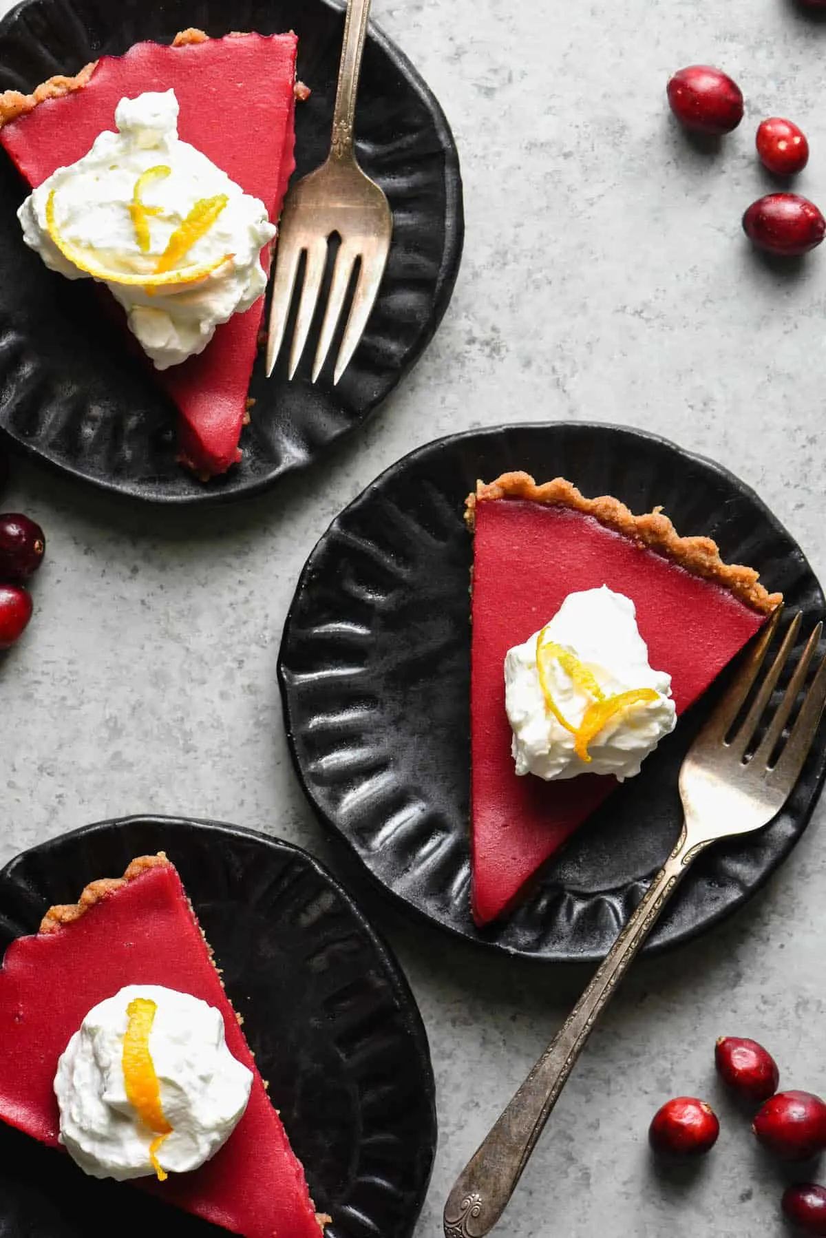 Three black plates each of them with a slice of overhead cranberry curd tart.