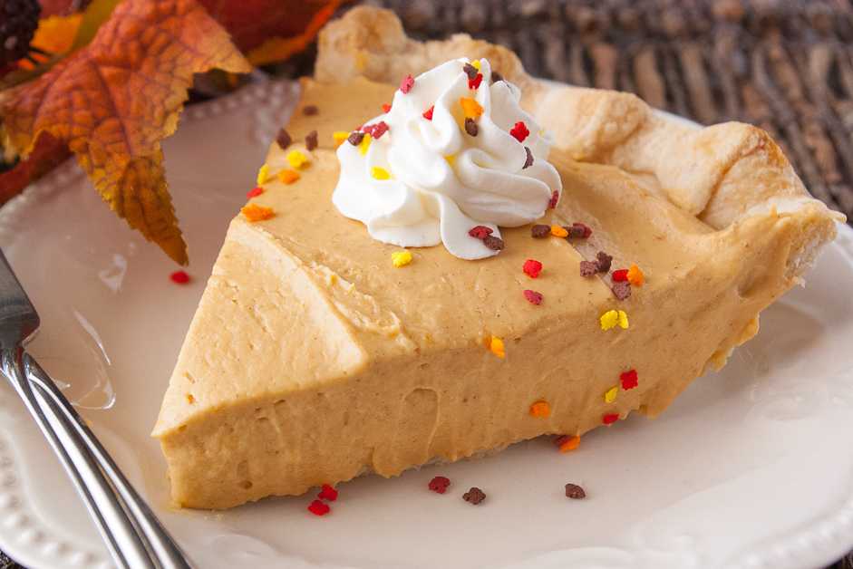 A big slice of pumpkin cream pie with whipped cream and colorful toppings.