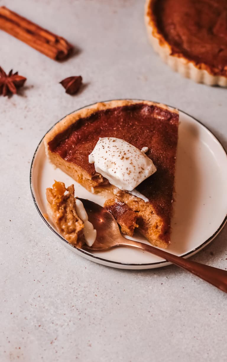 A slice of sweet potato pie on plate, star anise and cinnamon stick in the background.