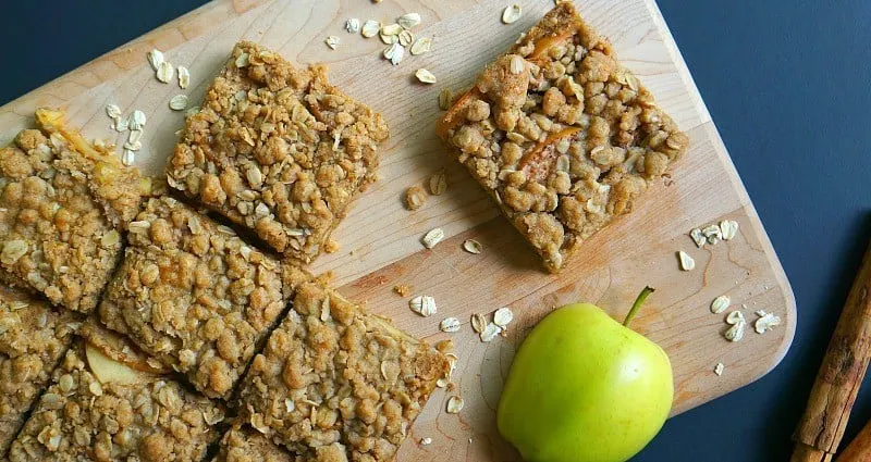 Apple oat bar cut in squares on a chopping board next to a green apple.