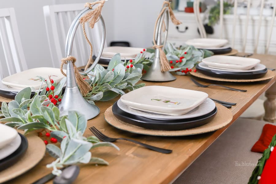 A table setting for the holiday with holly centerpiece on a wooden table.