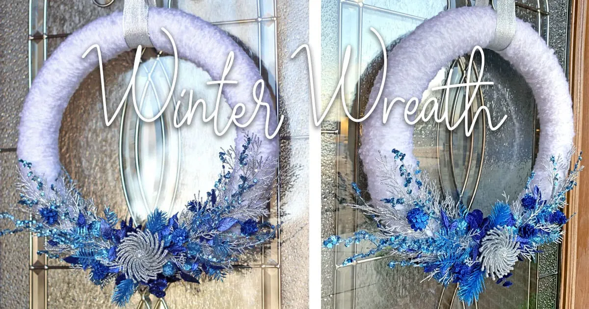 White wreath with blue branches and berries hanging from a glass door.