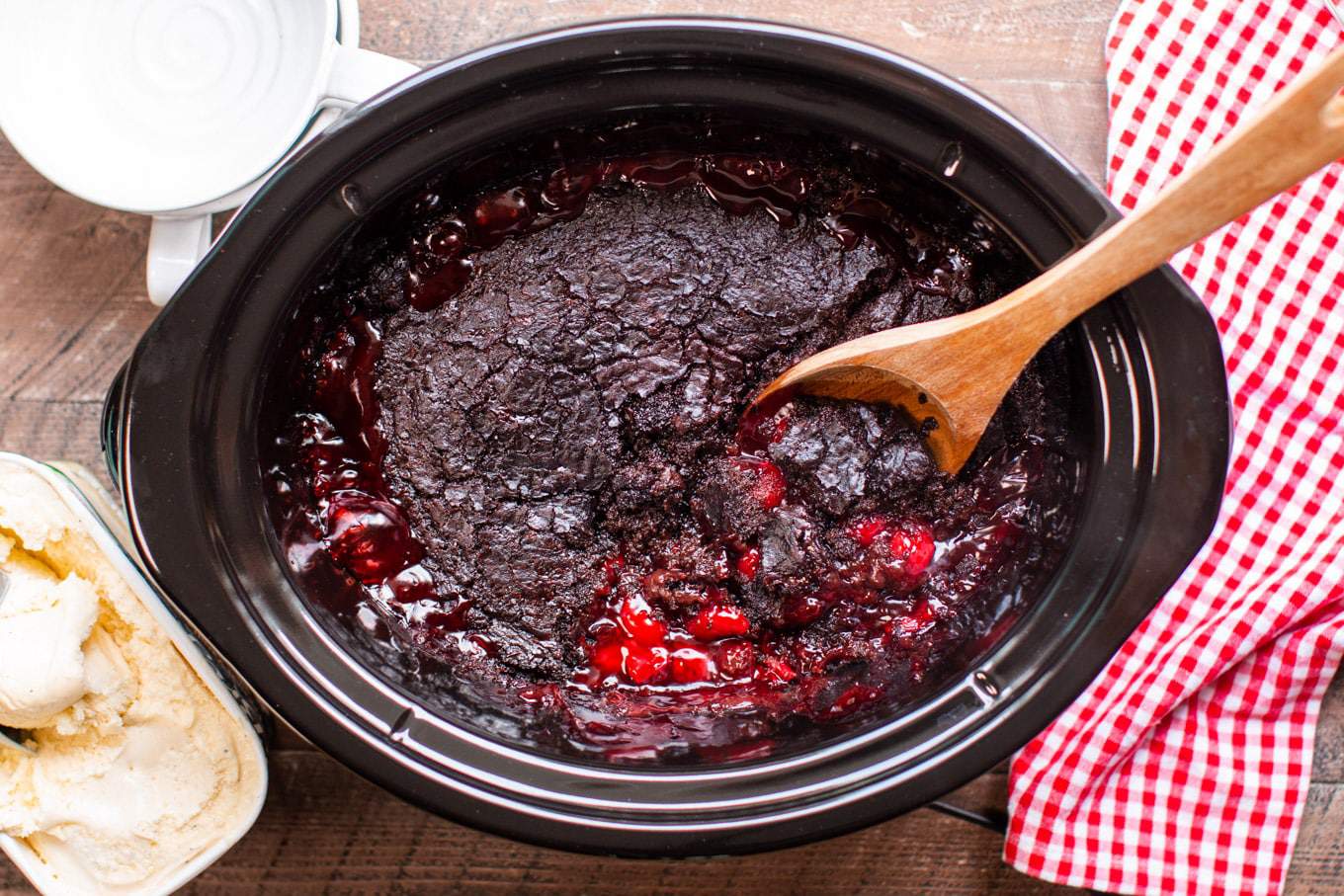 Crockpot chocolate cherry cake with a wooden spoon next to a red checkered table napkin.