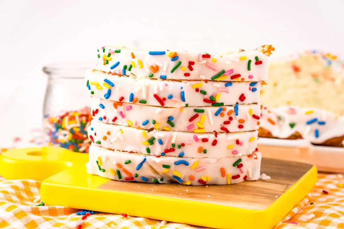 A stack of funfetti white cake with sprinkles on a yellow chopping board.