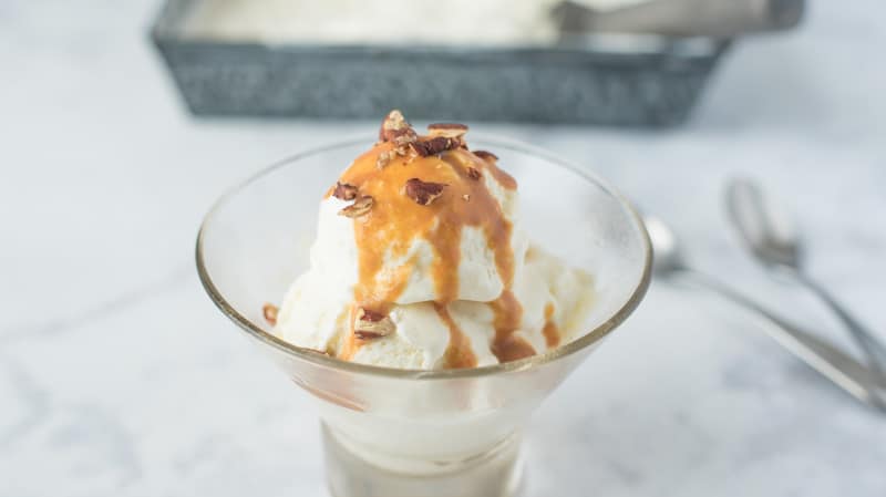 Scoops of vanilla ice cream with caramel and nuts toppings in a glass dish.