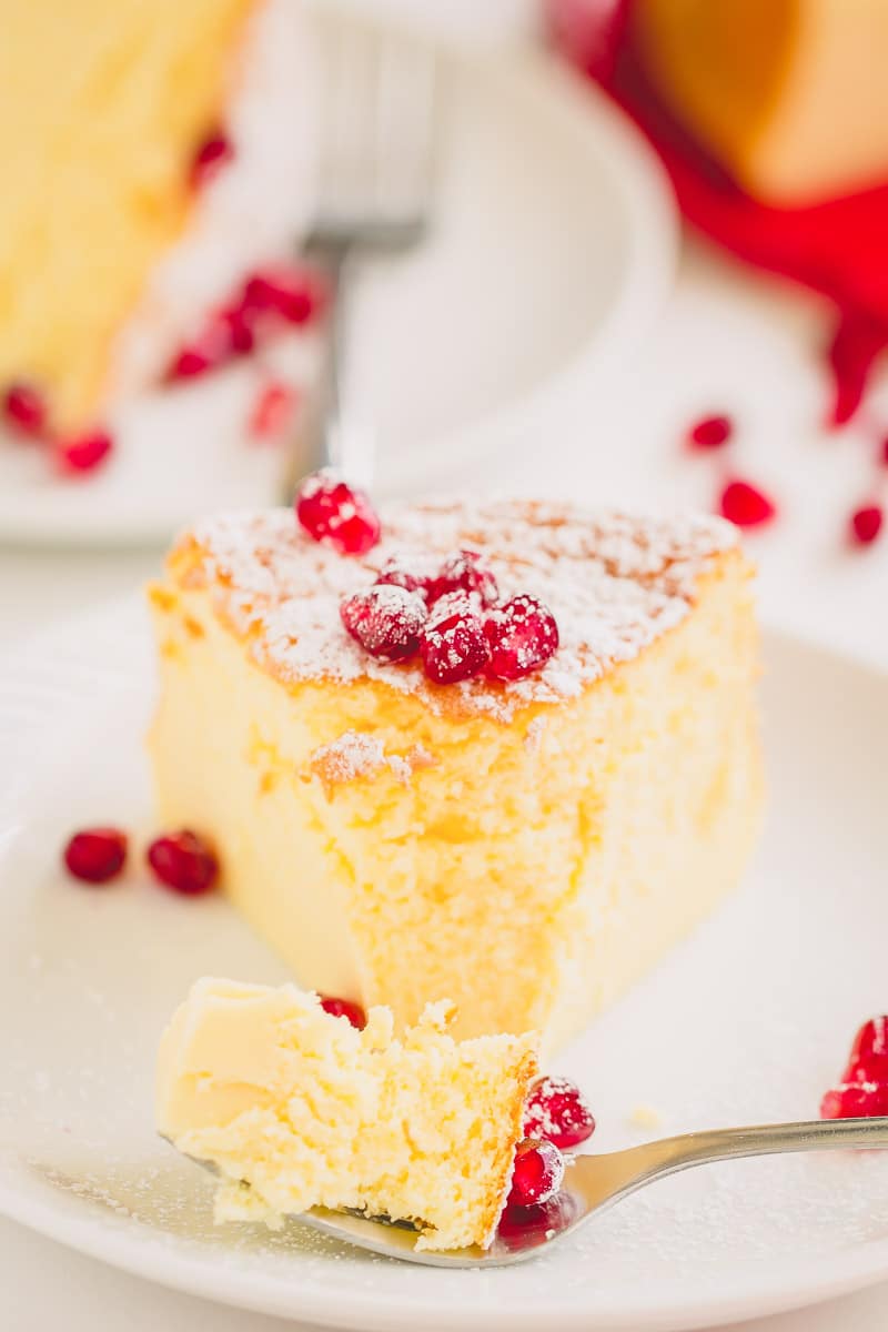 A slice of cheesecake garnished with powdered sugar, with a bite on the fork, on a white plate.