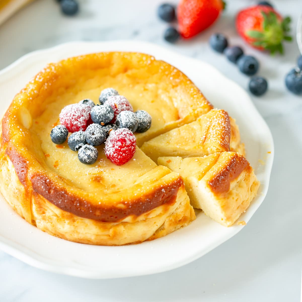 A whole crustless Italian ricotta cheesecake, two slices cut, garnished with red and blueberries.