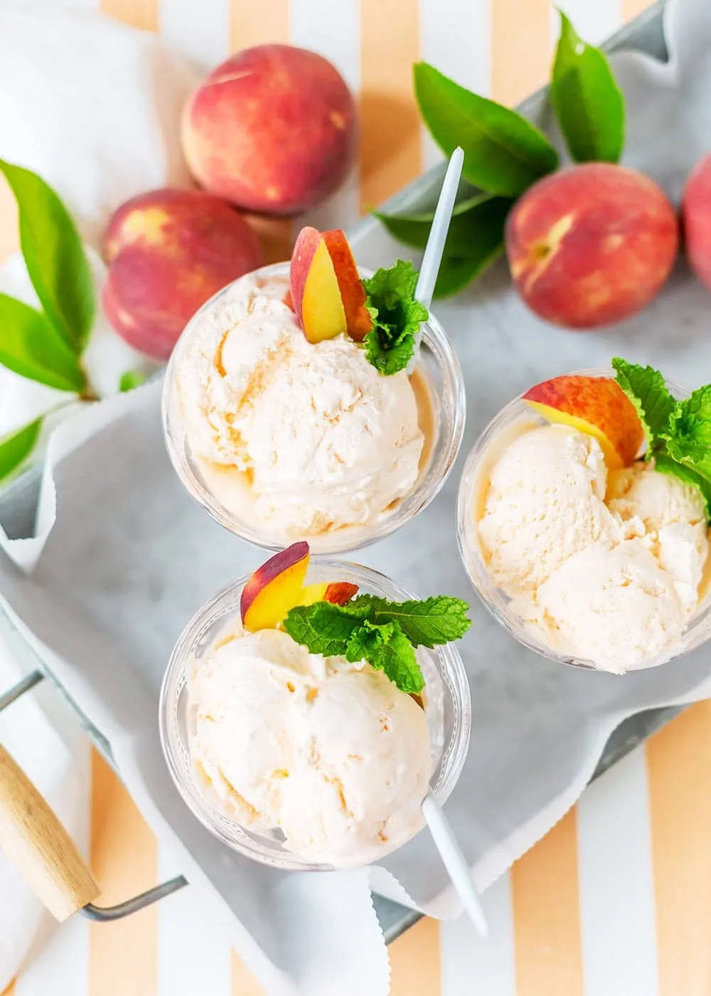 Three bowls of peach ice cream with fresh peach slices and mint garnish in a tray.