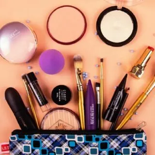 Different kinds of make up and brushes coming out from a blue make up bag.