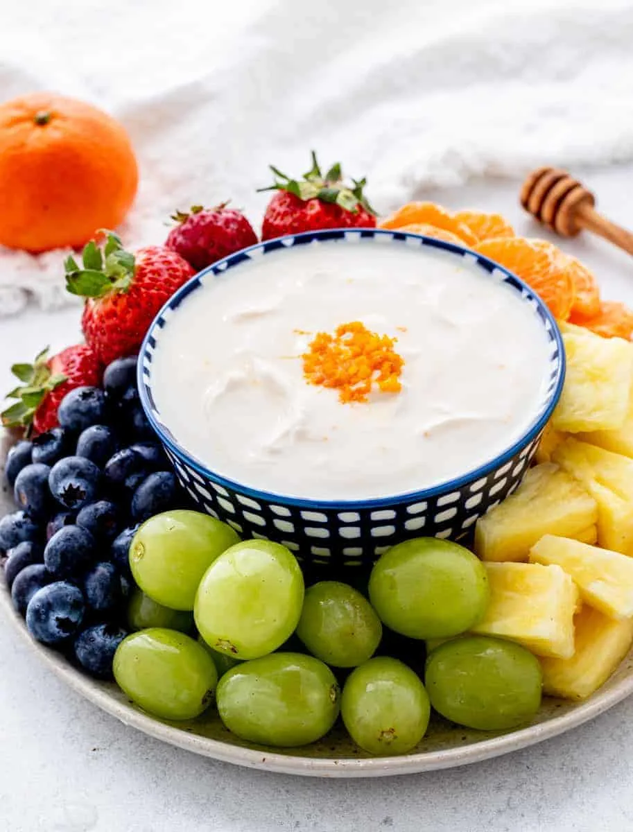 Green grapes, blueberries, strawberries, pealed oranges and sliced pineapples on a plate with yogurt dip in the middle.