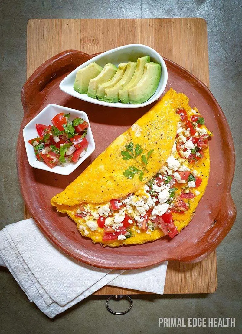 Mexican omelette with avocado slices and salsa sides on a plate placed on top of a wooden board.