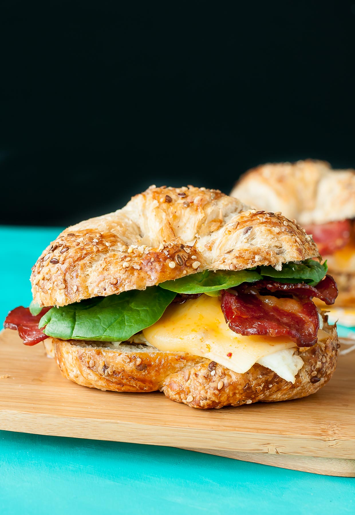 Croissant breakfast sandwich with egg, lettuce and bacon placed on a wooden chopping board.