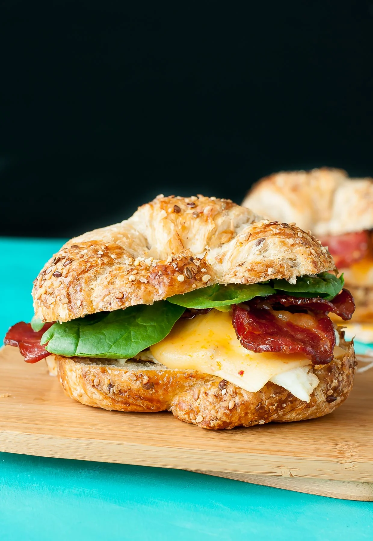 Croissant breakfast sandwich with egg, lettuce and bacon placed on a wooden chopping board.