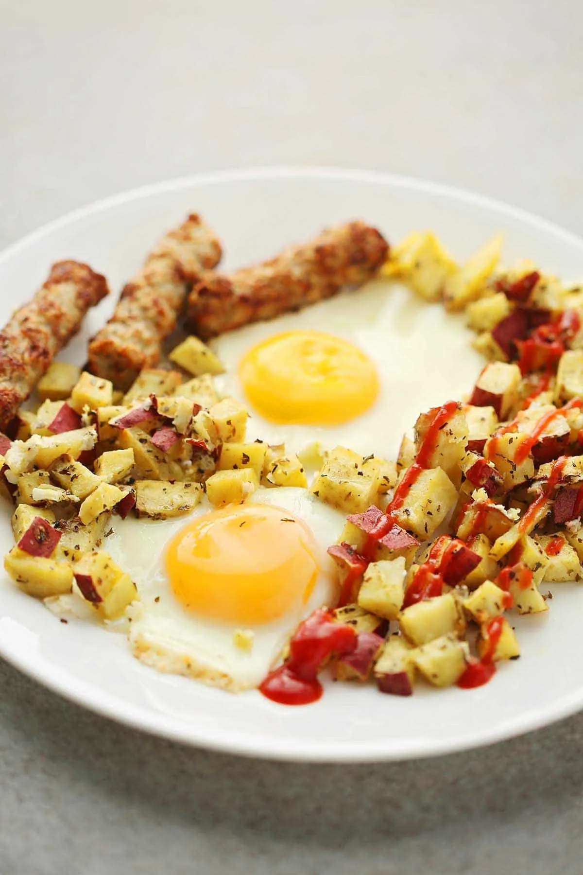 Eggs potato sausage on a white plate with ketchup.
