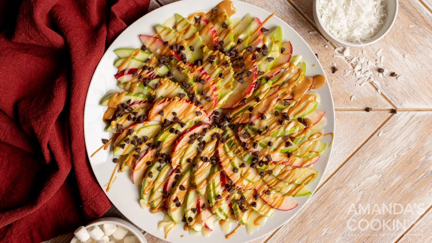 Apple nachos drizzled with caramel and chocolate chips on a white plate.