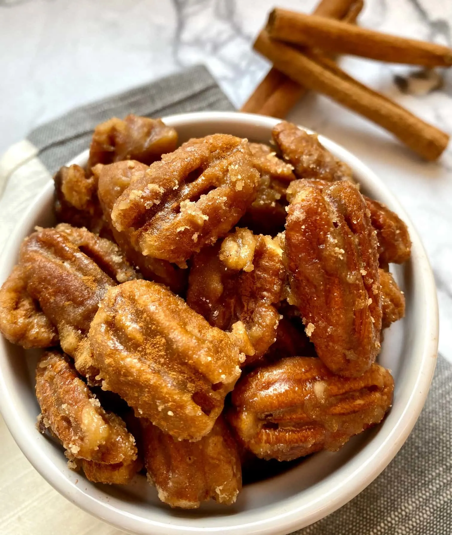 A bowl of candied pecans next to cinnamon sticks.