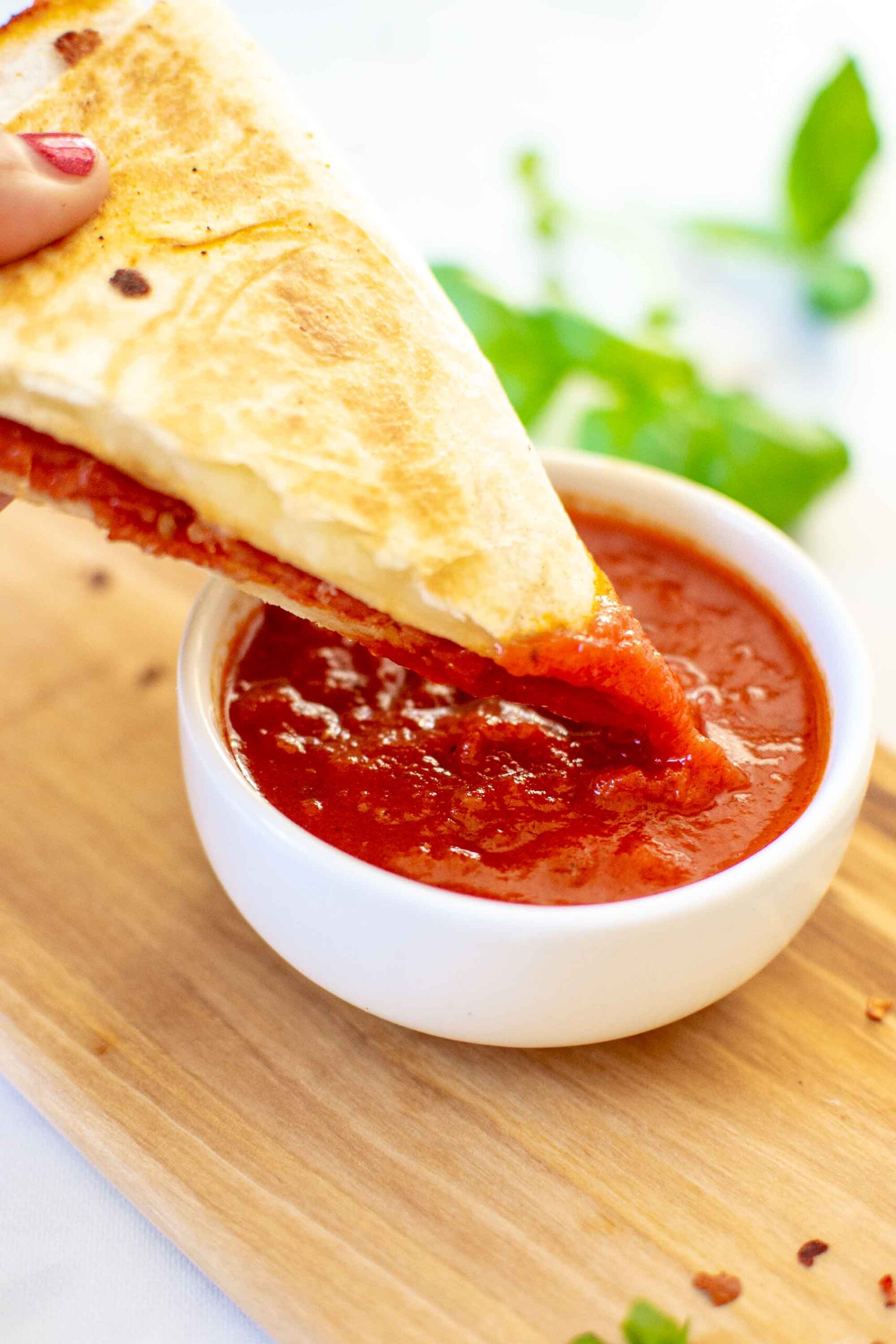 A person holding a slice of pizza wrap and dipping it into the pizza sauce.