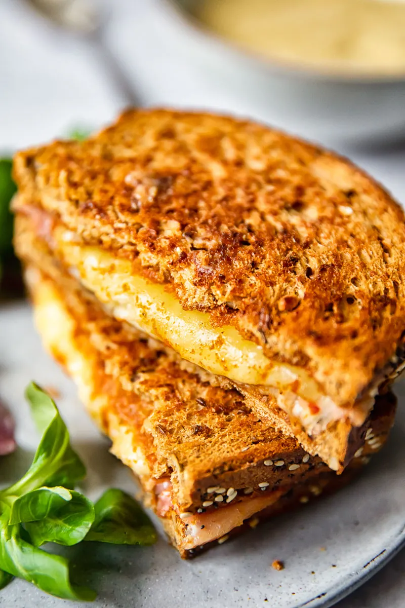 Two ham and cheese toasties stacked together on a plate.