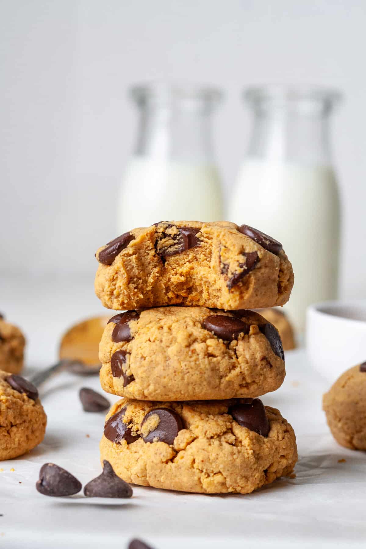 Three protein chocolate chip cookies stacked together with two bottles of milk in the background.