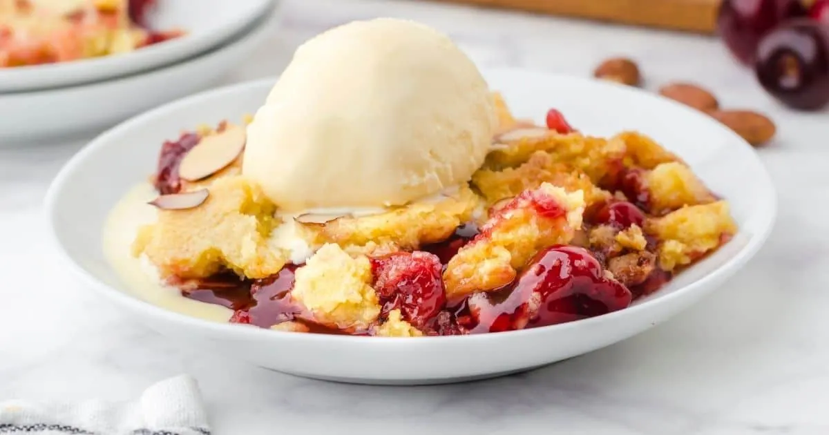 Cherry dump cake with a scoop of vanilla ice cream on a white bowl.