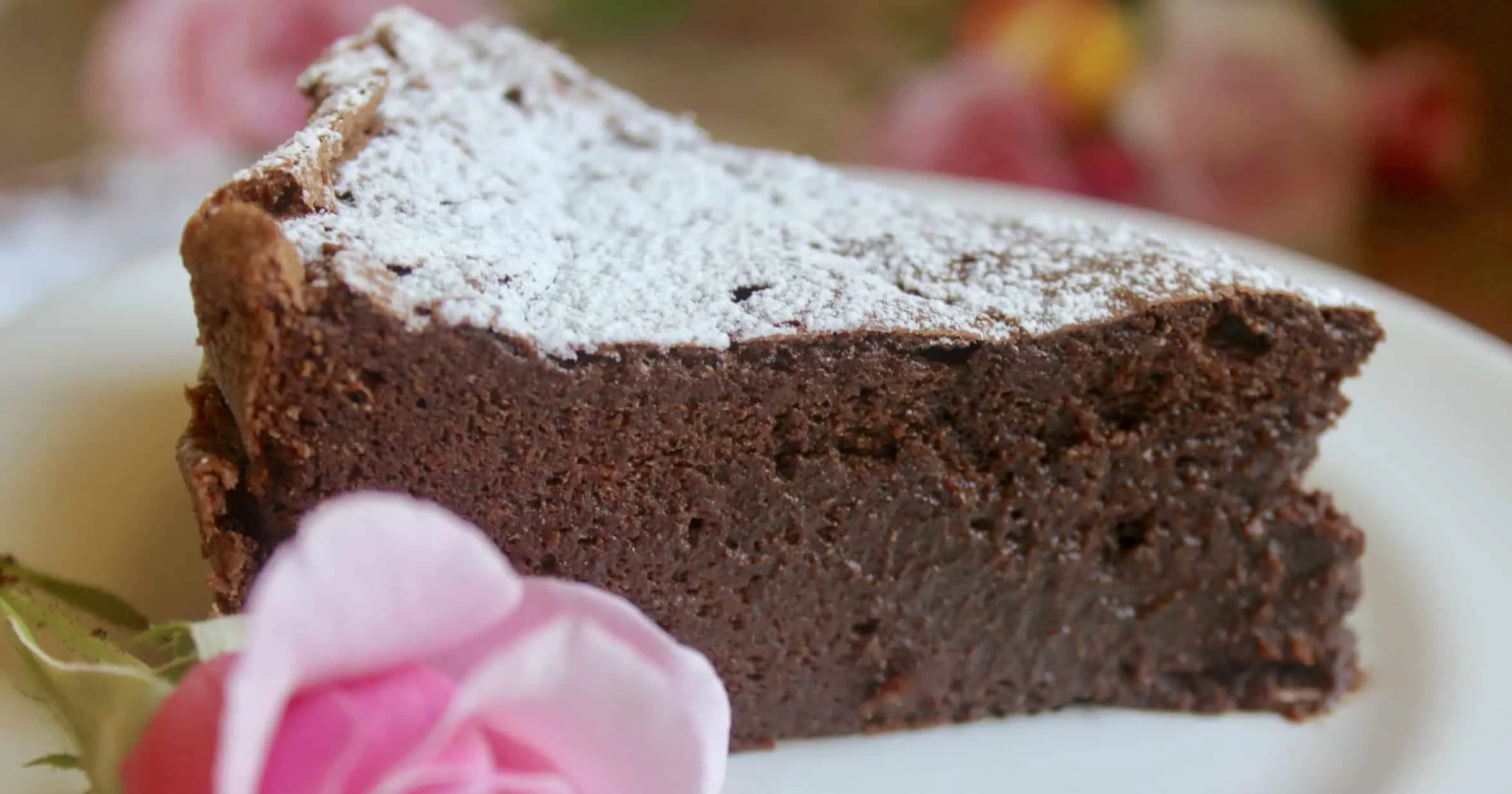 A slice of chocolate torte garnished with powdered sugar on a plate with a pink rose.