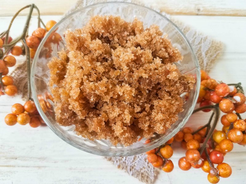 Pumpkin spice sugar scrub in a glass bowl decorated with fall-colored berries.