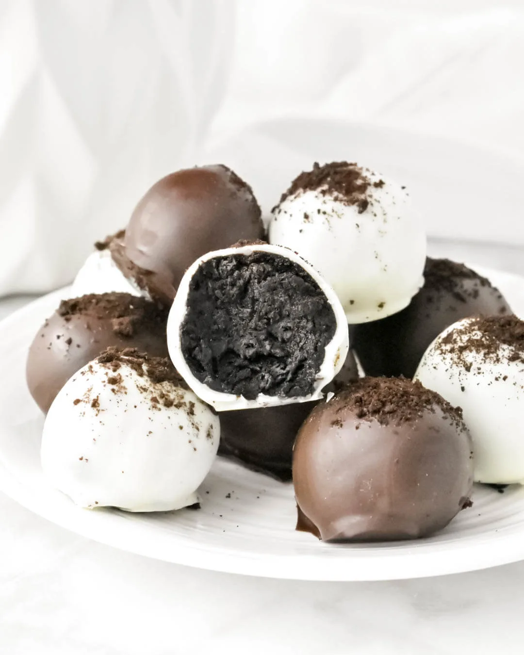 No-bake black and white balls of oreo truffles chocolate cream cheese on a white plate.