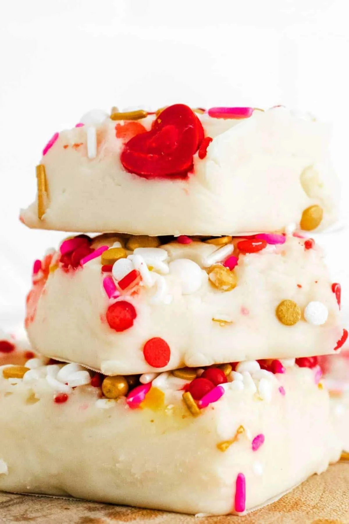 A stack of three white chocolate fudge with red, pink and gold sprinkles.