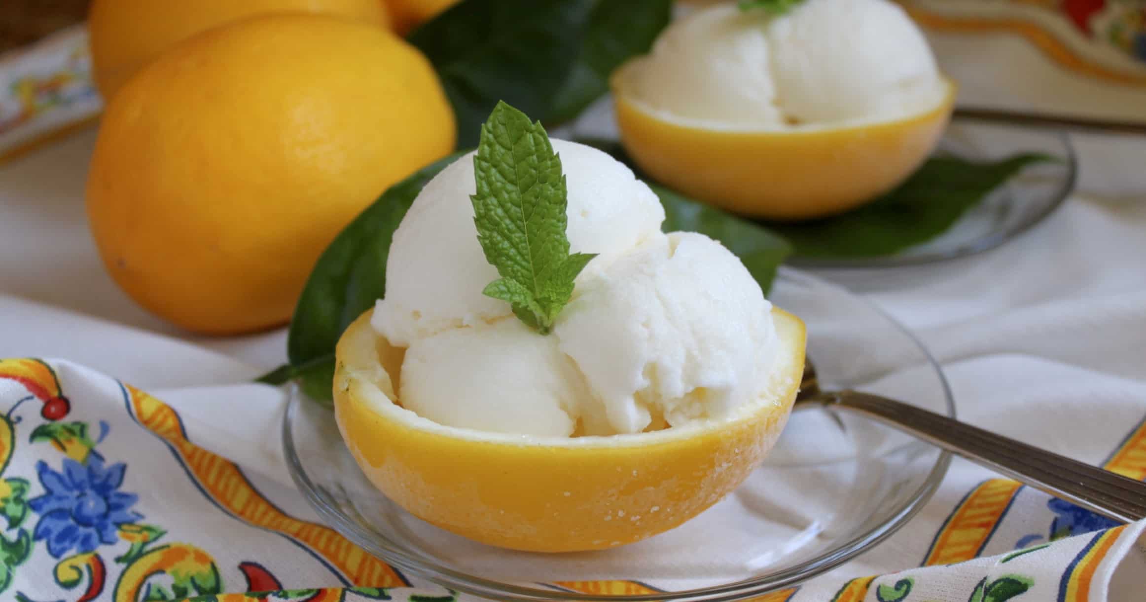 Lemons cut in half and filled with ice cream and topped with mint leaves as garnish on a clear glass plate with a spoon.