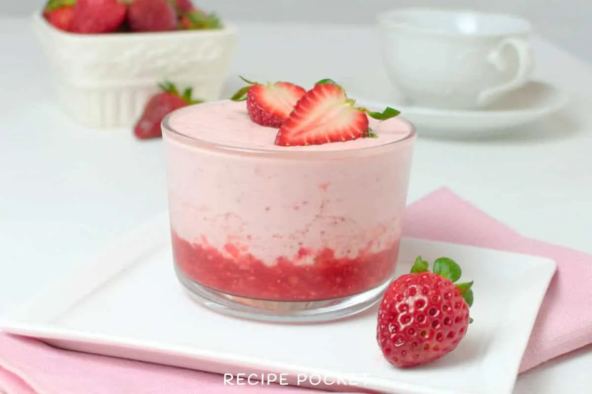 Strawberry fool in a glass dish next to a piece of fresh strawberry.