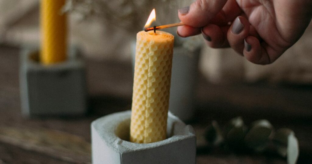 A person lighting a rolled beeswax candle in a concrete holder.