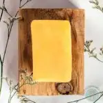 A bar of turmeric soap on a wooden board surrounded by tiny flowers.