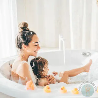 A woman and a little girl enjoying a bubble bath with three rubber duckies on the side of the bath tub.