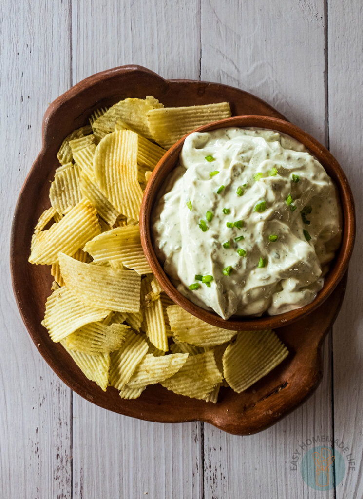 A bowl of lawson's chip dip on a clay plate with chips on top of a white table.