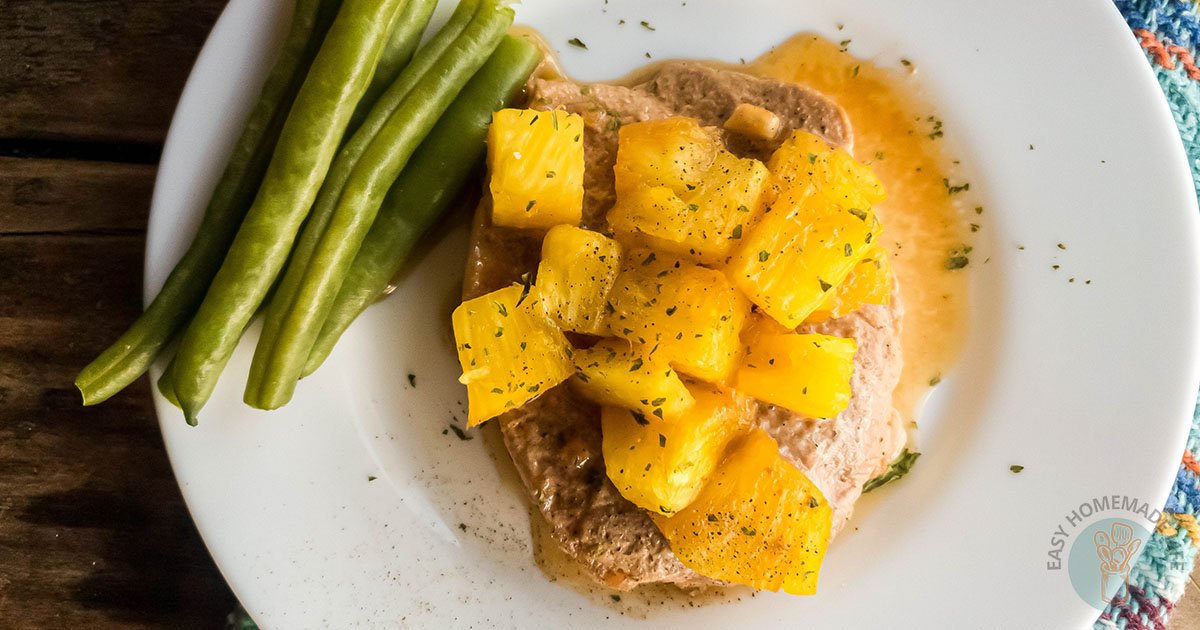 Oven baked pork chop with pineapple and green beans, white plate wooden background.