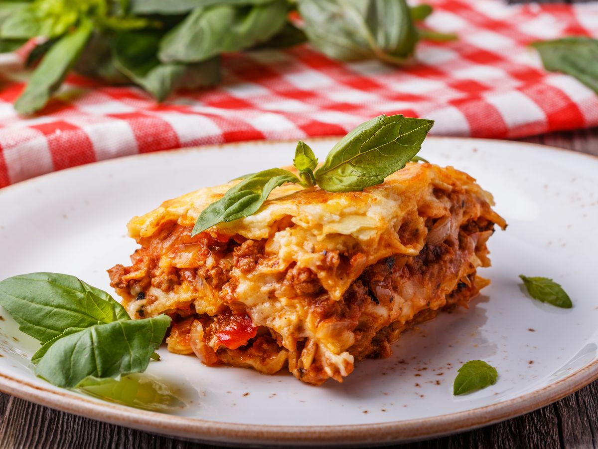 Lasagna portion on a white plate with basil leaves.