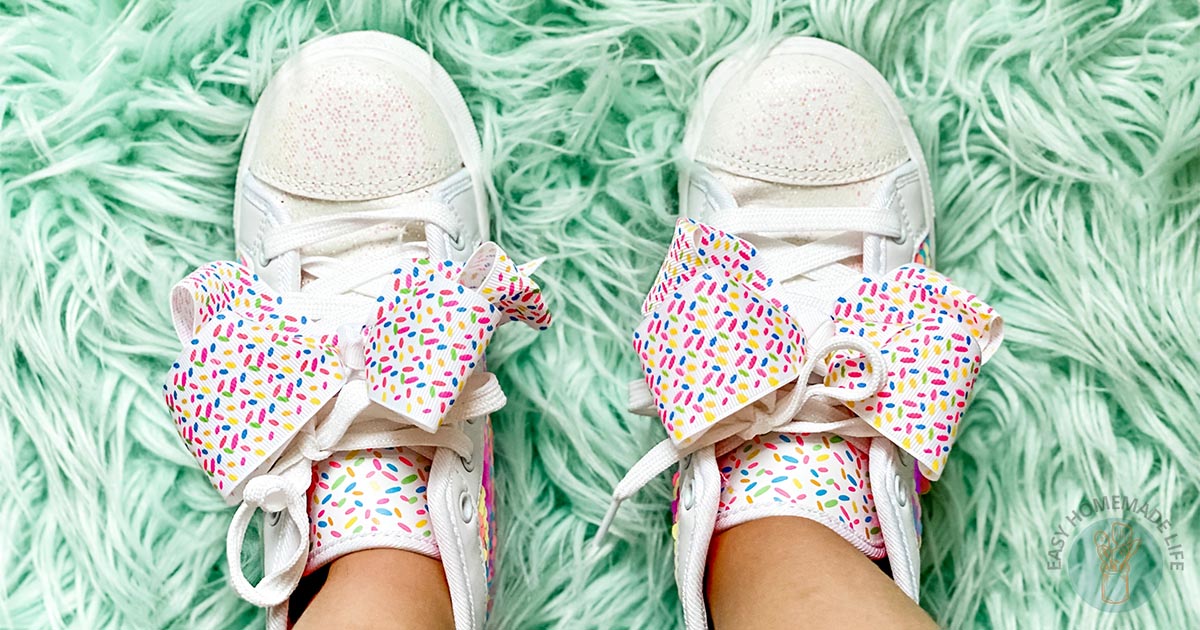 A little girl's white tennis shoes with oversize bow on green shag rug.