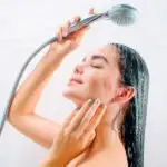 Woman with blue nails holding shower head over head.