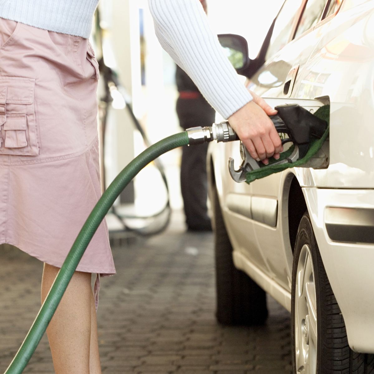 Woman pumping gas at station in pink skirt.