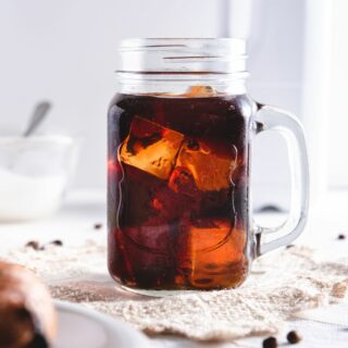 A mug of cold brew coffee with burlap cloth and coffee beans on table.