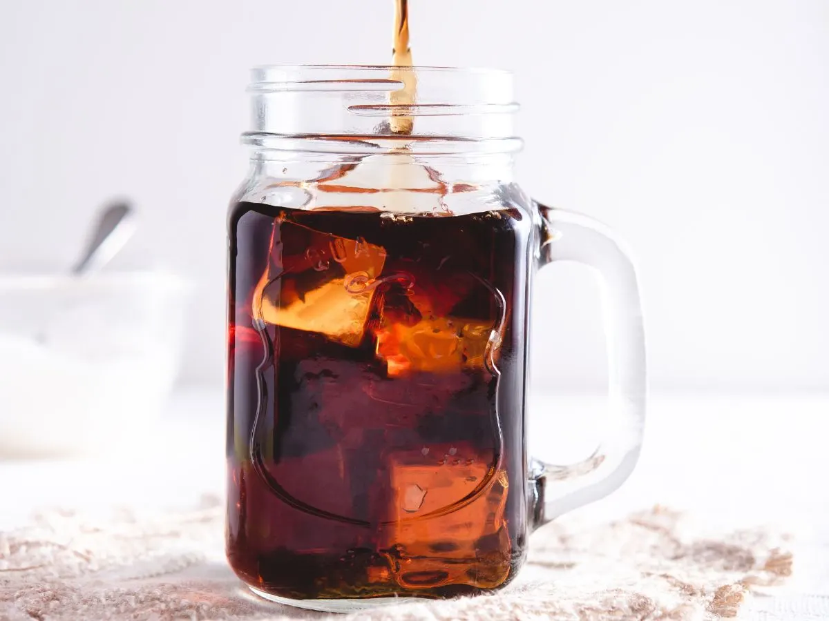 Pouring cold brew into glass mug with ice.