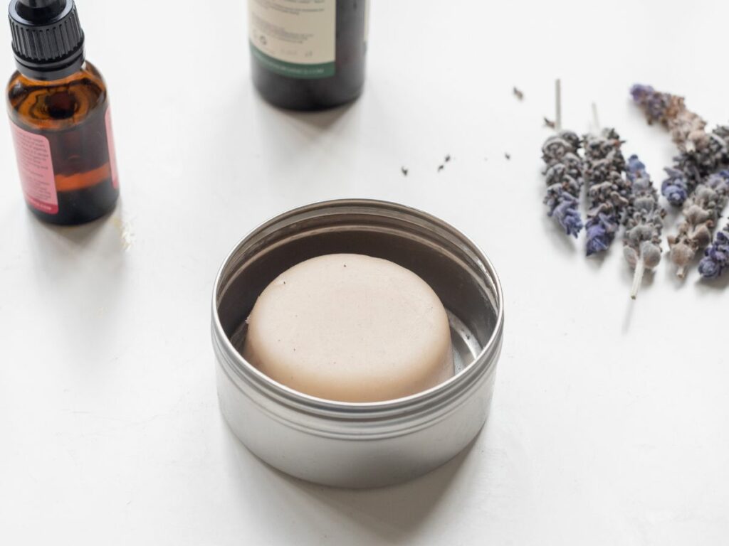 Essential oil bottles and lavendar flowers with lotion bar in metal tin.