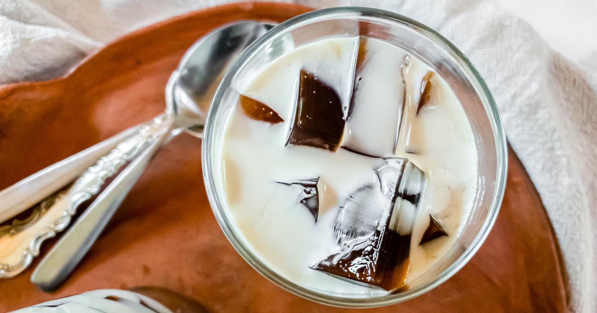 A glass of coffee jelly with heavy cream on a fabric background.