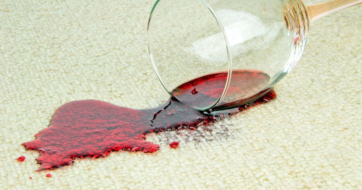 A wine glass tipped over, spilling red wine on the carpet.