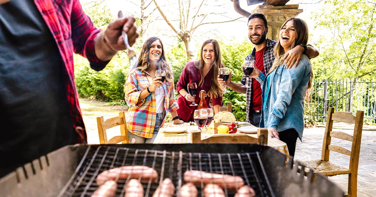 A backyard BBQ with friends grilling sausages on a grill.