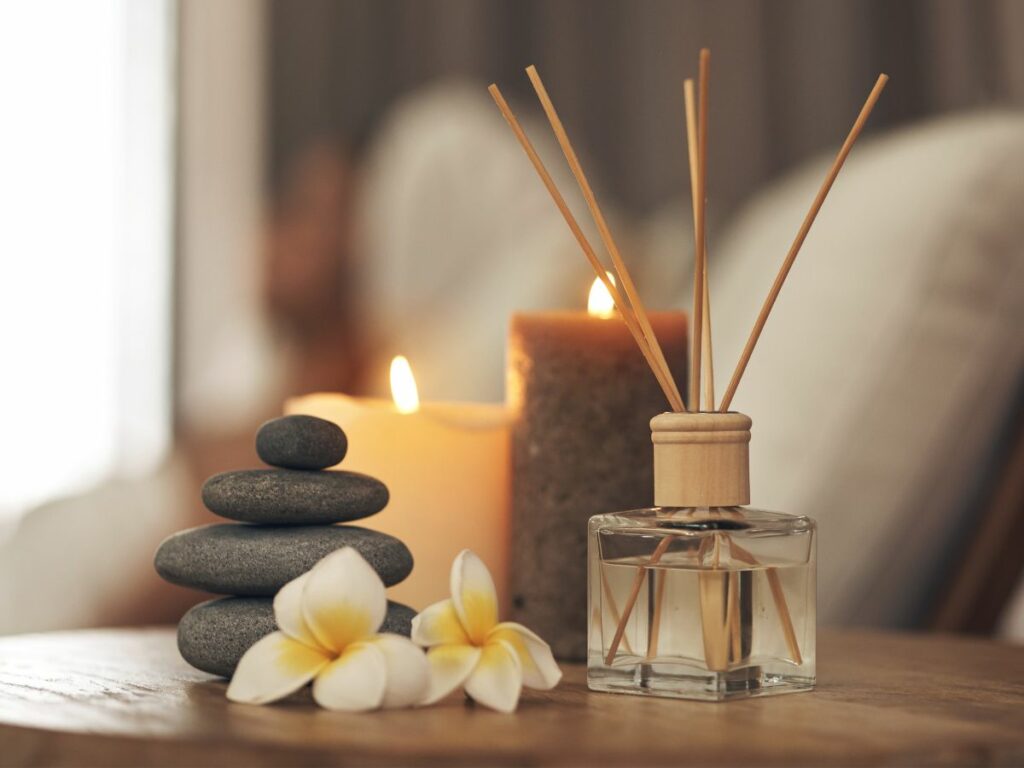 Reed diffuser with flowers and candles on a table.