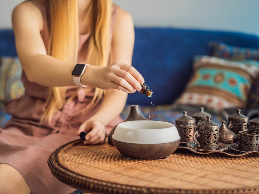 A woman is pouring essential oils into a diffuser on a table.