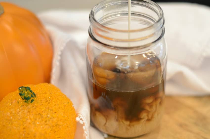 A mason jar filled with coffee next to pumpkins.