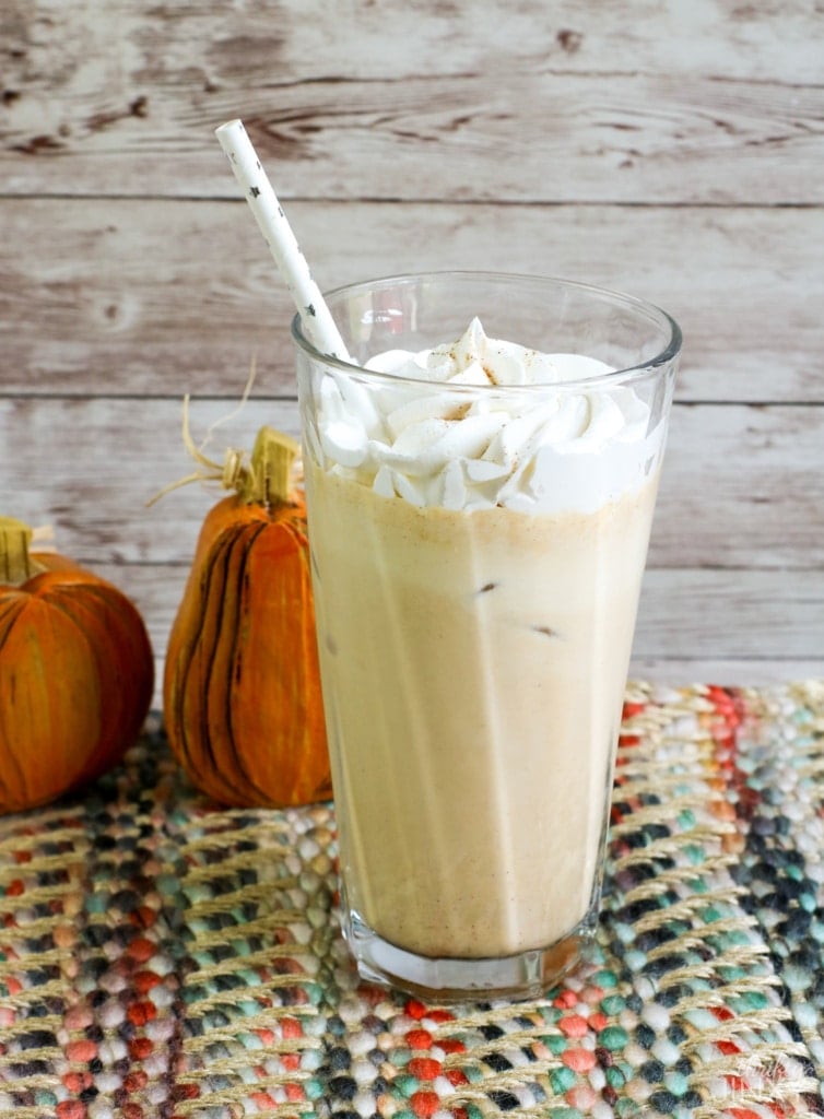 A glass of pumpkin spice latte with whipped cream next to pumpkins.