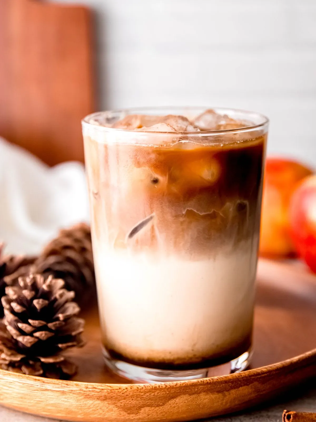 A glass of iced coffee with apples and pine cones.
